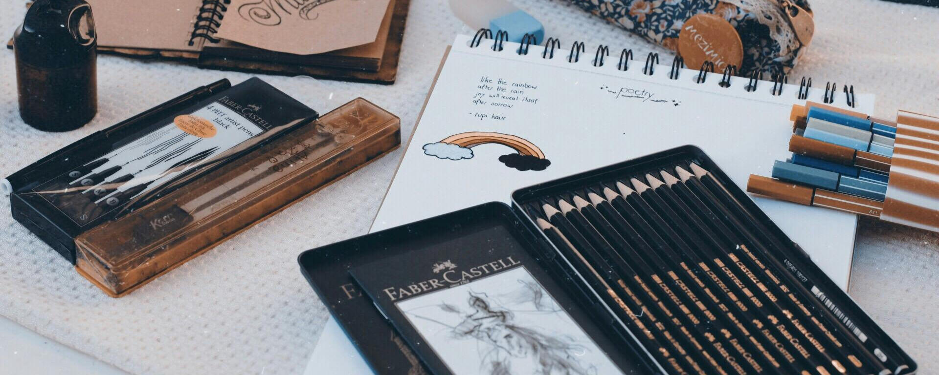 Picture of a black, rectangular tin pencil case filled with black pencils and markers on top of a notepad