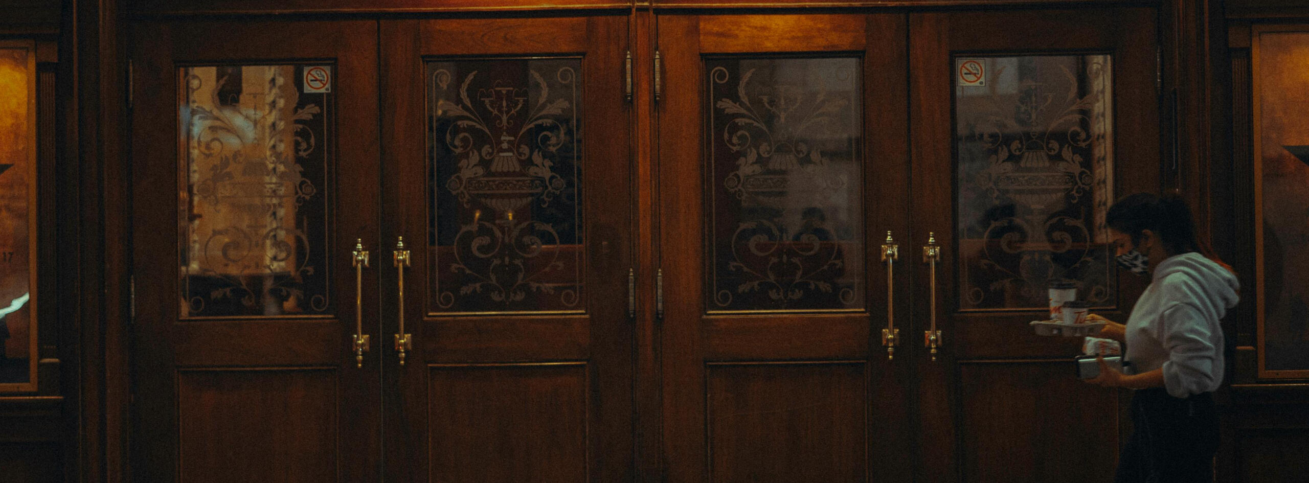threshold picture of a woman walking past a set of doors while holding a tray of cups of coffee